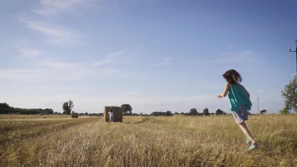 Two Cute Little Girls Push a Roll of Mown Rye in a Field in Summer