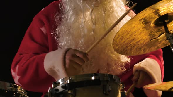 Cheerful Musician Dressed As Santa Claus Plays Drums on a Black Studio Background alt