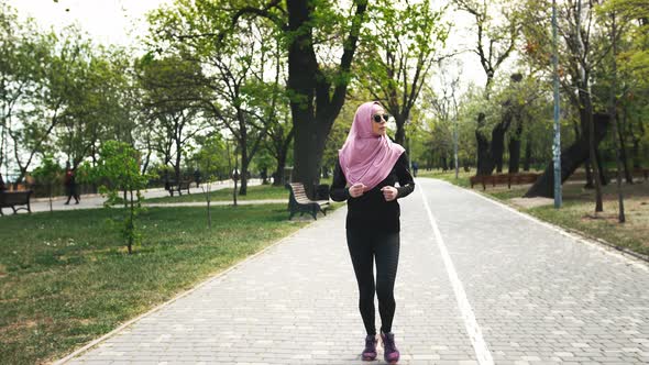Young Modern Muslim Woman in Sunglasses and in Hijab Jogging in Green Park alt