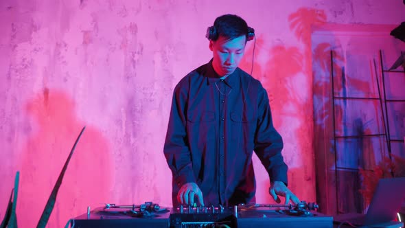 Modern DJ of Asian Appearance Performs a Music Track in Neon Lighting alt