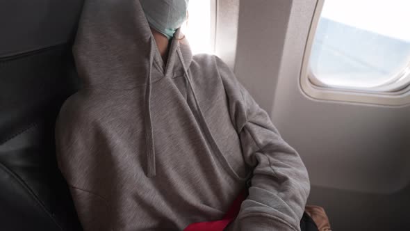 Tired Woman Passenger in Covid Safety Face Mask Sleeping in Seat at Window in Airplane alt