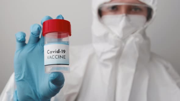 Doctor in Protective Suit Face Mask Safety Googles and Rubber Gloves Demonstrate Vaccine Against alt