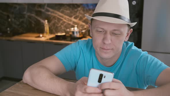 Portrait of an Attractive Man Who in a White Hat Sits at a Table Uses a Mobile Phone alt
