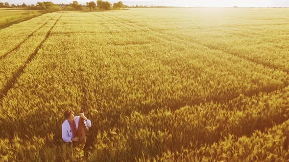 Aerial Shot of Romantic Musician in Vyshyvanka Playing on Bandura in Wheat Field Under Sunset
