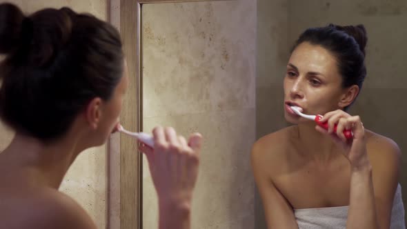 Beautiful Woman with Cream on Face Washes Teeth in Front of Mirror alt