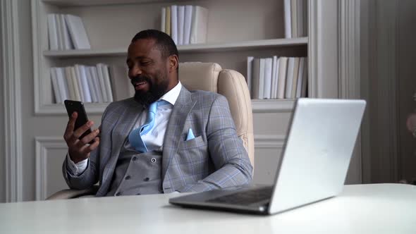 a Bearded AfricanAmerican Man in a Plaid Suit with a Tie is Sitting at a Table on a Light Chair and alt