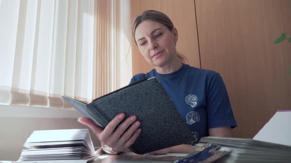 Woman Looks Through Old Family Photos in Album and Reminisces About Past Time alt