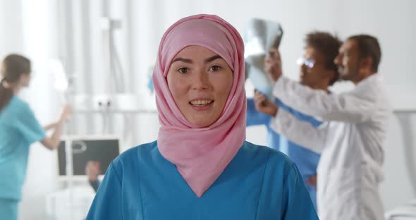 Portrait of Muslim Doctor in Scrubs Standing at Hospital Talking at Camera alt