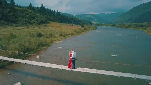 Couple Stands on Bridge Over a Mountain River. Love of Man and a Woman alt