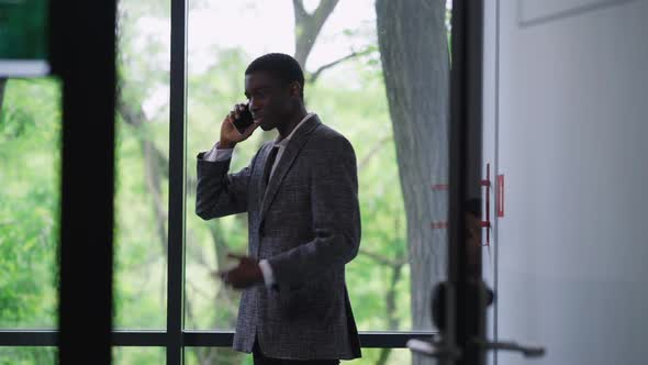 Nervous Stressed African American Young Man Arguing on Phone in Office with People Passing at Front alt