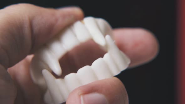 Person Plays with Funny Vampire Teeth on Black Background alt