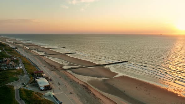 Beautiful aerial shot of a beach with wooden groins to prevent erosion, at high tide during sunset alt