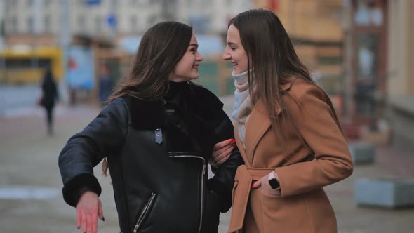 A Friend Comes Up From Behind Her Waiting Girlfriend on a City Street alt