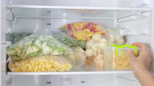 Female Hands puts containers with frozen vegetables in the fridge.