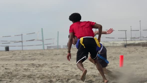 A group of guys playing flag football on the beach. alt
