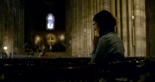 Lady Prays Against Blurry Illuminated Cross in Darkness alt