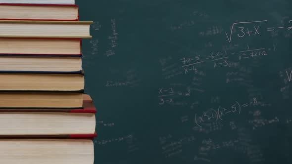 Stack of books against mathematical equations on black board alt