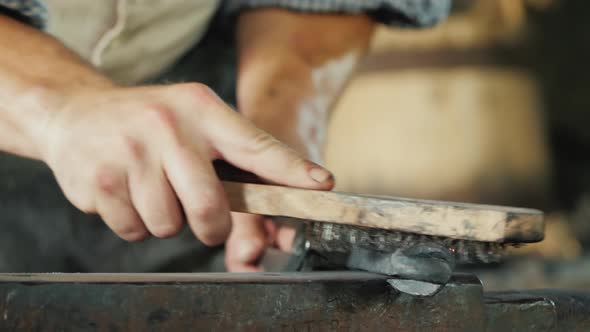 A Blacksmith with a Metal Brush Cleans the Workpiece From Scale and Debris alt