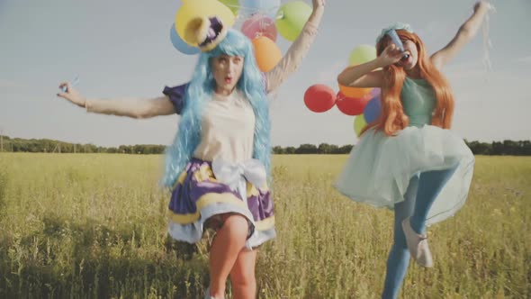 Two Cheerful Girls in Bright Costumes of Princesses and with Balloons Are Having Fun in the Field