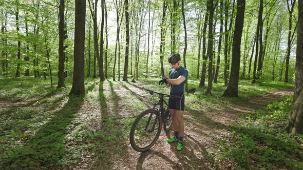 A Happy Cyclist is Standing in the Middle of the Forest and Looking at the Training Data on His alt