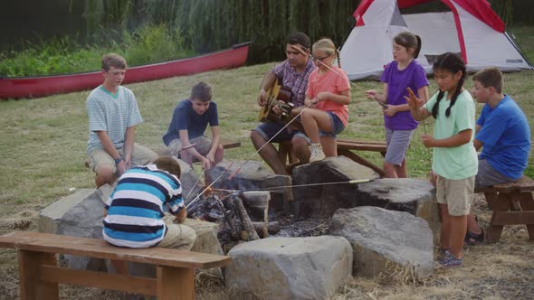 Kids at summer camp roasting marshmallows around campfire