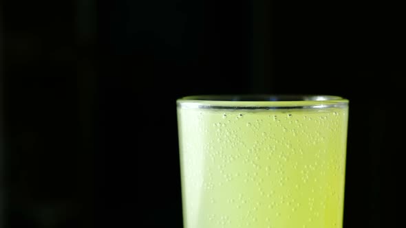  Half of Full Glass with Carbonated Yellow Drink on a Black Background