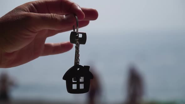 Keys with a Houseshaped Keychain in a Man's Hand on Sea Beach Background alt