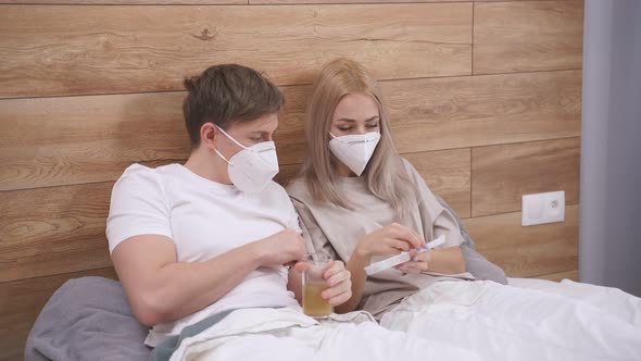 Couple in Medical Masks Taking Medications Pills Vitamins While Sitting on Bed Suffering
