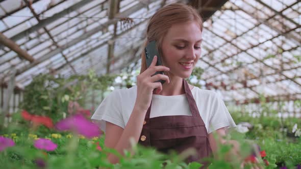 Close Up Portrait of Beautiful Joyful Female Florist Store Manager Talking on Cellphone About Plant