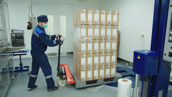 Loader in Protective Mask and Uniform Pushing Cargo Trolley Manually at the Pharmaceutical Plant