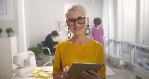 Mature Businesswoman Using Tablet Computer in Studio of Startup Fashion Business alt