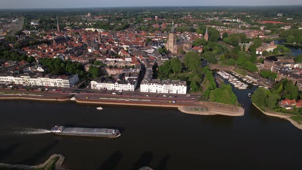 Medieval city seen from above with inland shipping large cargo vessel leaving ripple waves on river alt