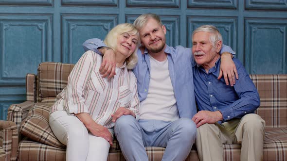 Family of Senior Grandparents with Adult Son Embracing Having Fun Looking at Camera Bonding at Home alt