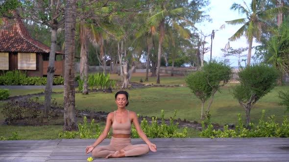 Meditating Yoga Trainer Woman Sitting in Lotus Pose on the Path in Tropical Resort Wellness