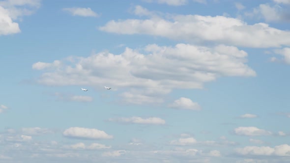 Two White Planes Fly Side By Side on City Against Background of Blue Sky and White Clouds