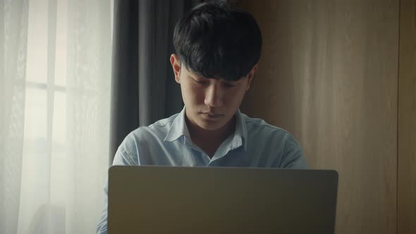 Young Attractive Asian Vietnam Man Busy Work Computer or Smart Tablet on Laptop at Home in Freelance alt