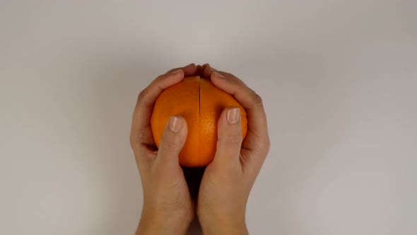 Beautiful female hands open cut orange in studio lighting