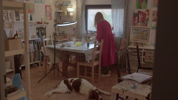 Woman with a Dog is Preparing for an Art Lesson in Her Home Studio alt