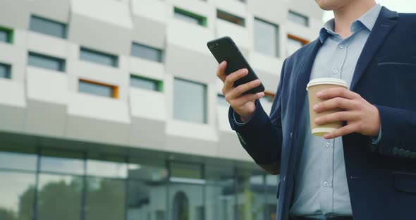 A Businessman is Walking Near the Business Center with a Cup of Coffee in His Hand alt