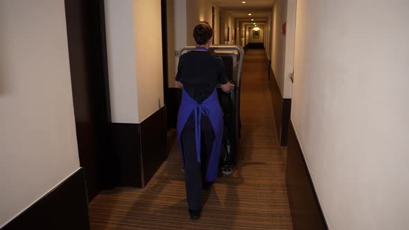 Cleaning Lady Driving Trolley Down Hotel Corridor alt