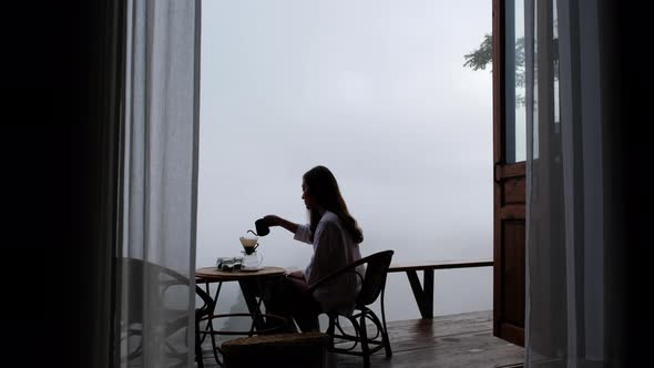 A woman making drip coffee with a beautiful nature view on foggy day