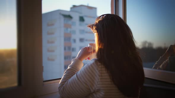 Woman Drinking Coffee on the Balcony at Sunset, Back View, Enjoying the Sunset alt