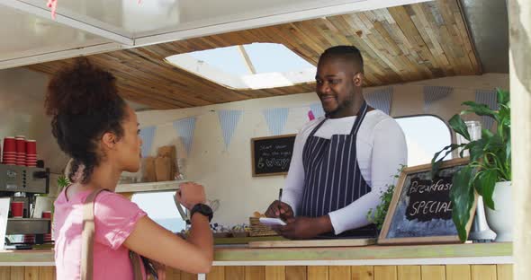Smiling african american male food truck owner taking order from happy female customer alt