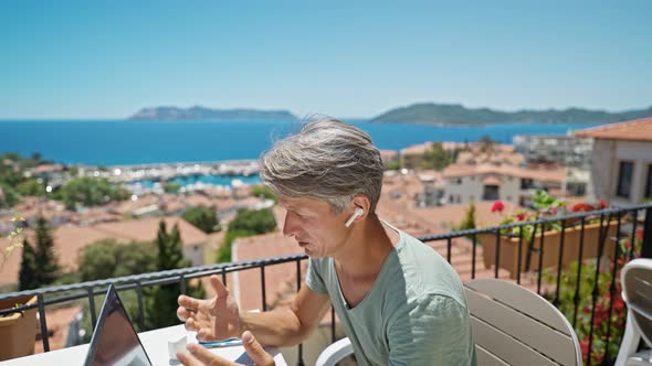 Dolly Zoom Footage Man in Erphones Working Witth Laptop Outdoors By Beautiful Blue Sea View Speaking alt