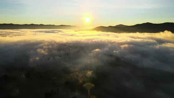 Aerial view of a small village houses on hill top in fall foggy mountains at sunrise. alt