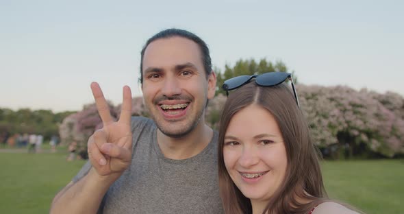 A Young Beautiful Couple of Tourists with Braces Make Selfies in the Park alt