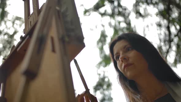 A Bottom View of a Beautiful Brunette Girl Doing Brush Strokes in a Painting. alt