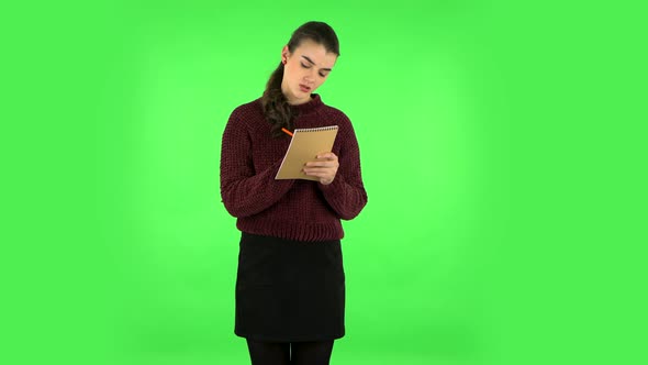 Girl Stands and Thinks, Then Angrily Writes with Pencil in Notebook. Green Screen alt