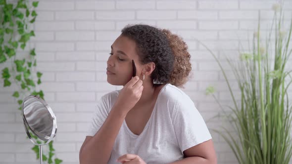 Young woman massaging face with gua sha stone at home alt