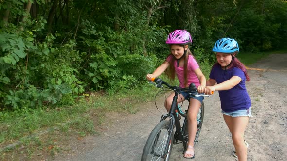 Two little girls in Bicycle helmets in nature. The older sister teaches the younger one how